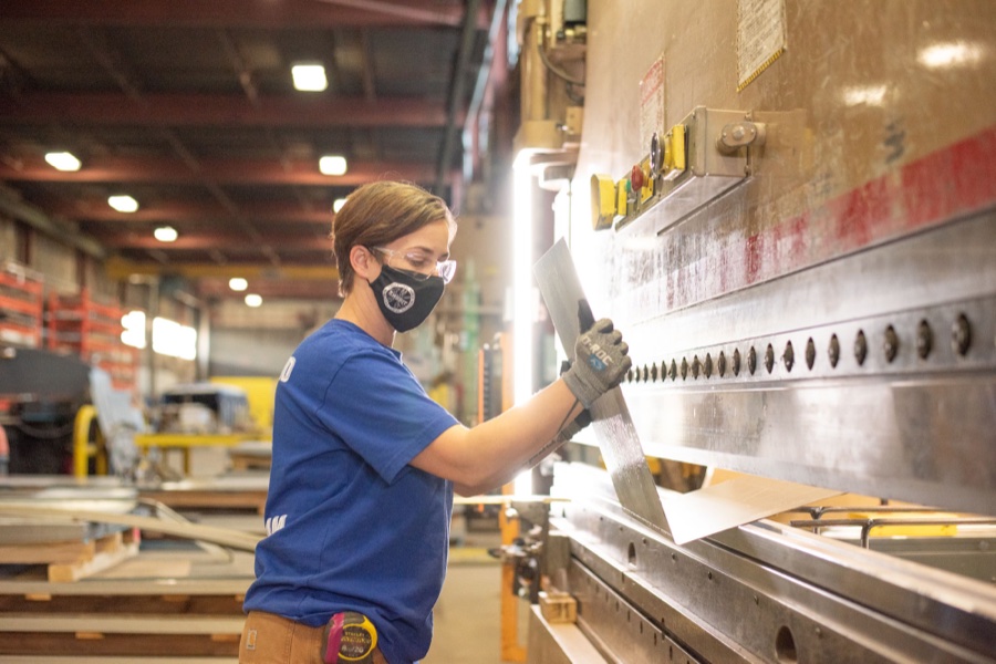 A woman operating a sheet metal press brake in a factory setting.